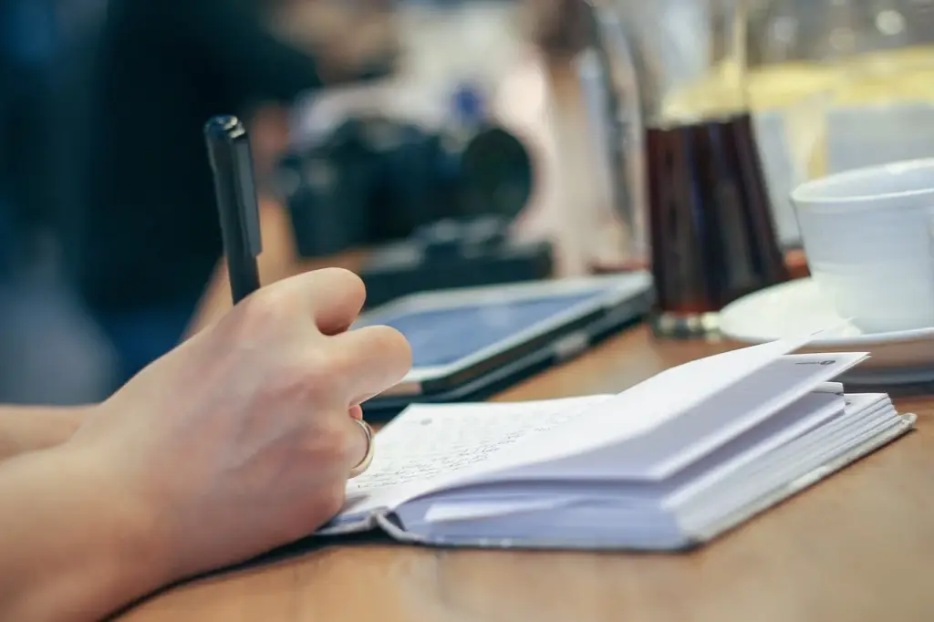 Person writing in a paper planner with a pen at a desk