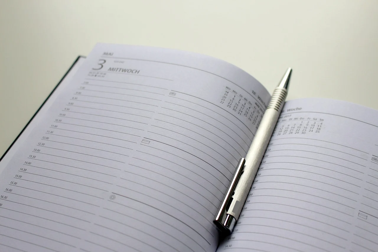 A person sitting at a desk with a planner and laptop, doing a weekly review